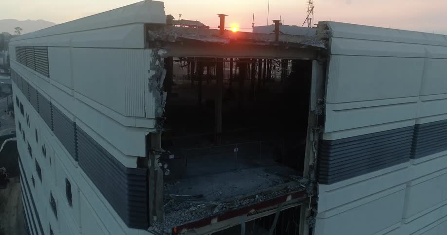 An aerial view of a large building missing a wall at sunset