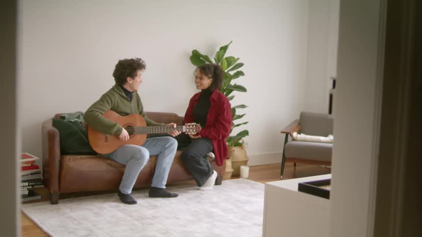 Young couple singing to an acoustic guitar tune while sitting in a couch at home