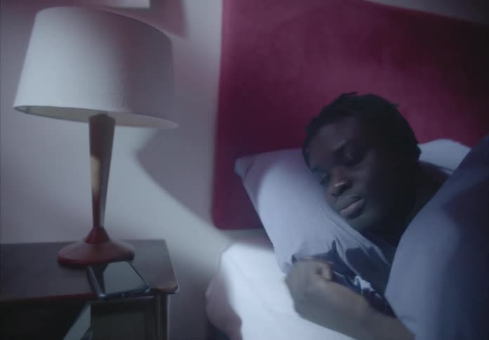 A black person laying in bed turns off phone and lamp