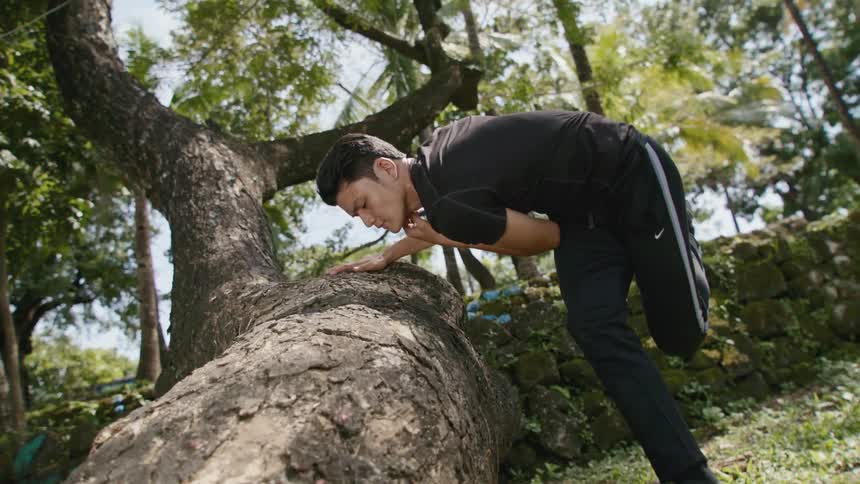 Man performing a dance near a tree trunk outdoors