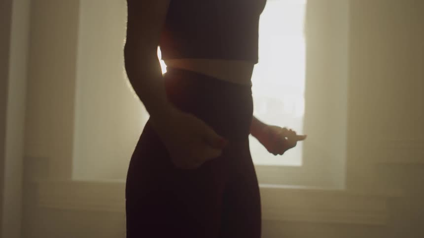 A woman in workout clothing shakes her hands and fingers as she walks past a window indoors