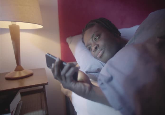 A man lies in bed and scrolls on his cell phone