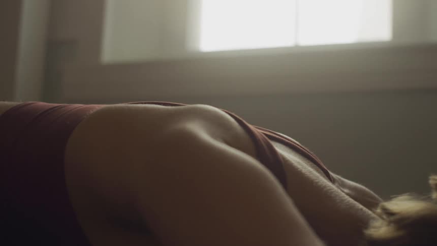 A woman stretched out in a yoga pose with her face lowered to the ground inside of a room at home next to a window at daytime
