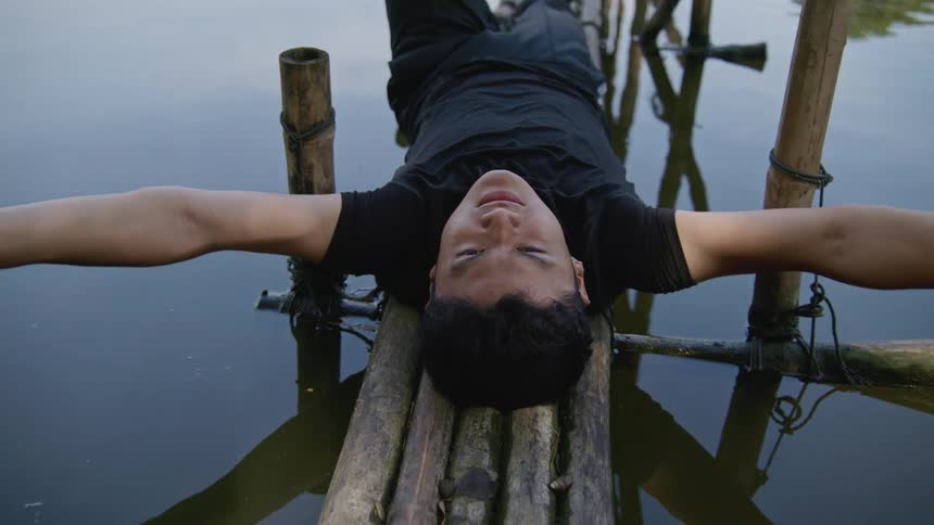 A male dancer lies on a raft and raises his arms