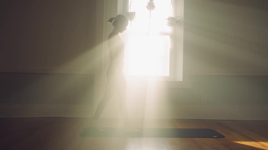 Woman lays the mat on the floor for working out while the sun shines through the window brightly in an empty room