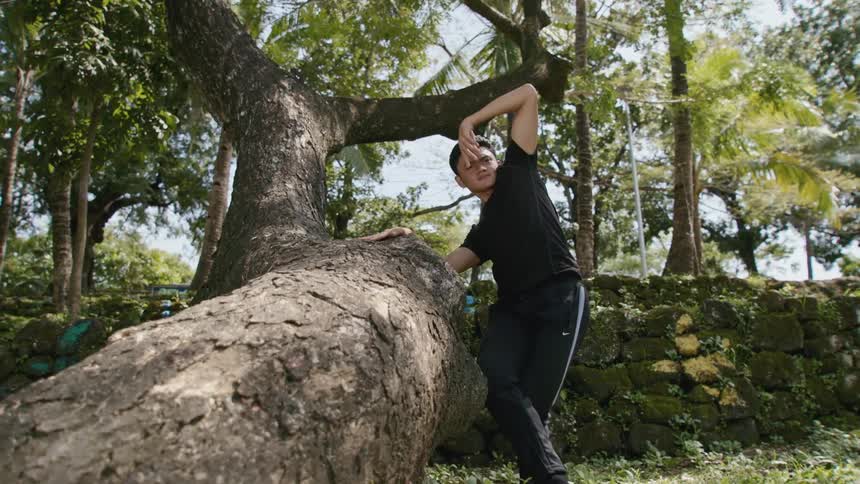 A male ballet dancer dancing beside a tree trunk outside