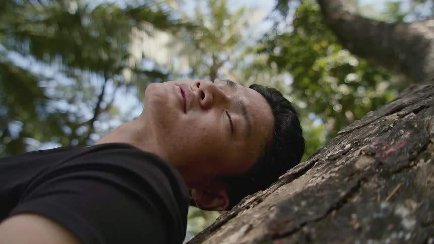 Man reclines against tree trunk closing his eyes