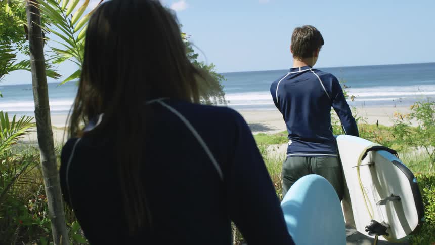 Two teenagers carrying surfboards walking on a path to a beach