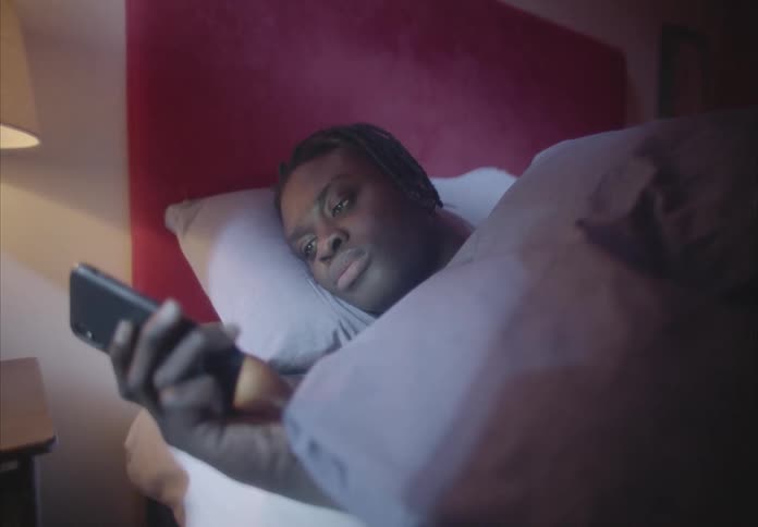 A man scrolling on a smartphone while lying in bed at night