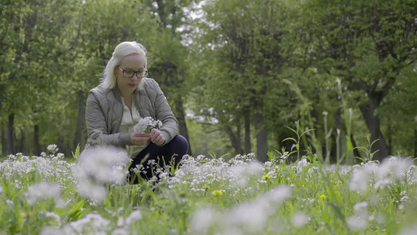 Woman gathering wildflowers in her hands in a peaceful meadow moment.