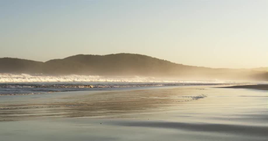 Waves roll in over a beach with a mountain in the distance