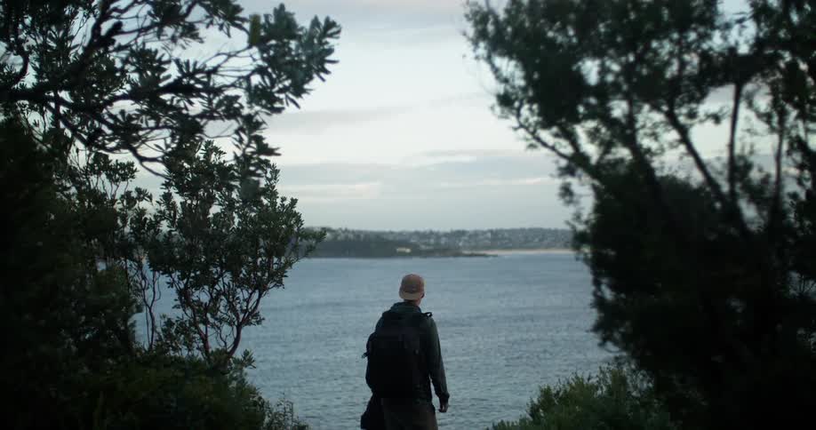A person with a hat and backpack standing by a lake with the sky and clouds in the background