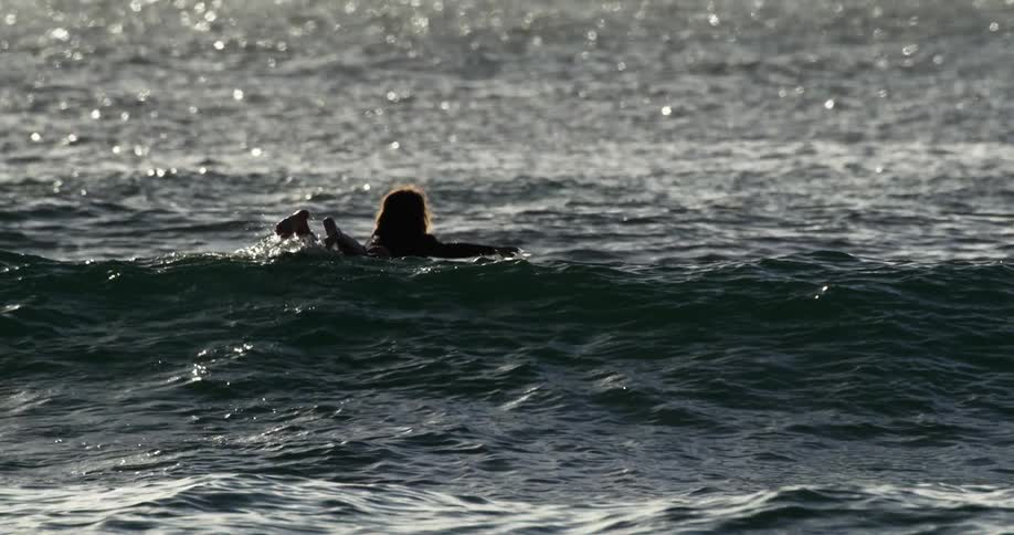 A woman laying on a surfboard on the ocean floating above waves of water