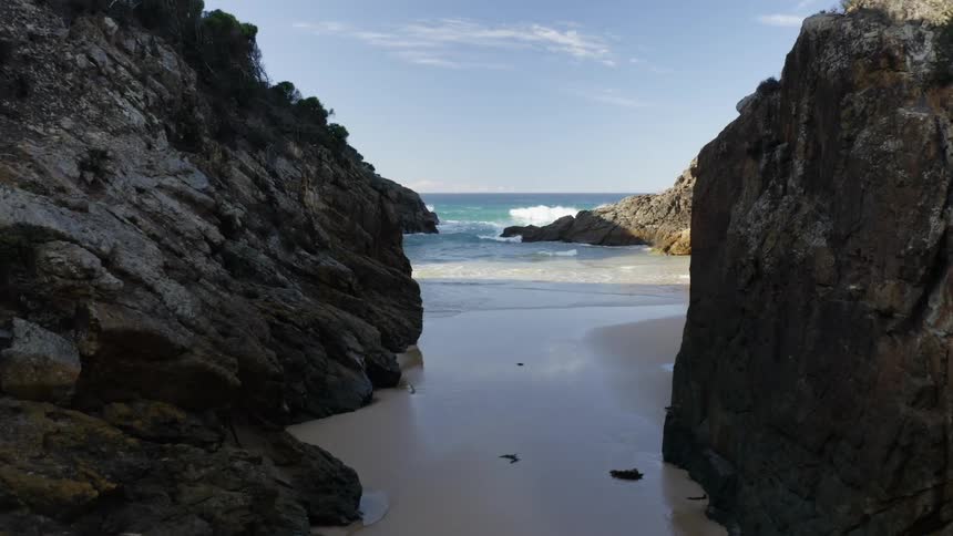 A passage between cliffs leading to a beach where ocean waves roll in on a sunny day
