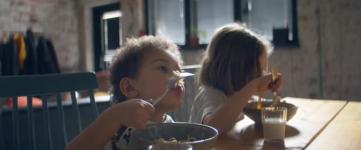 Two boys sitting at the table eat spaghetti at home