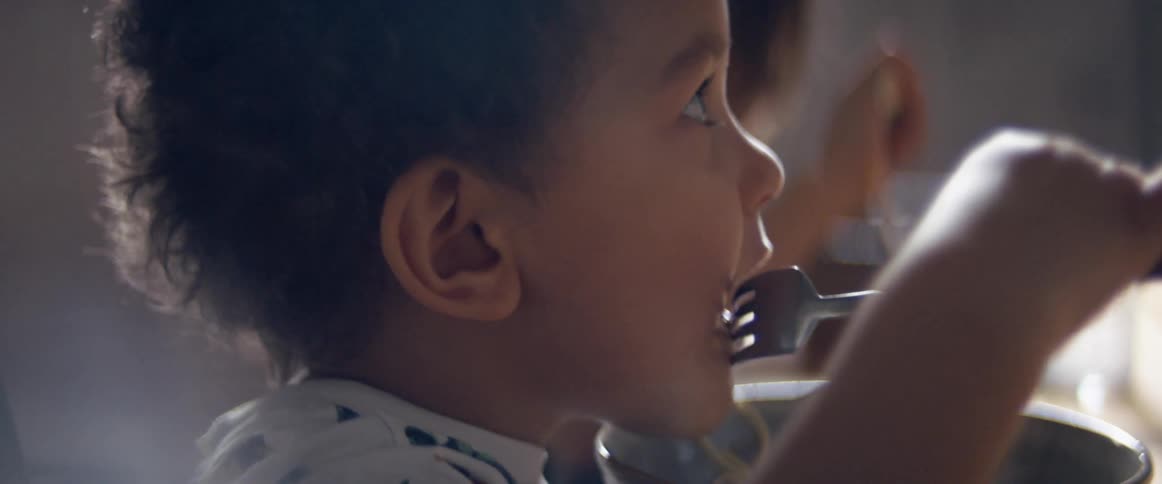 A toddler nodding their head while eating with a fork at a table