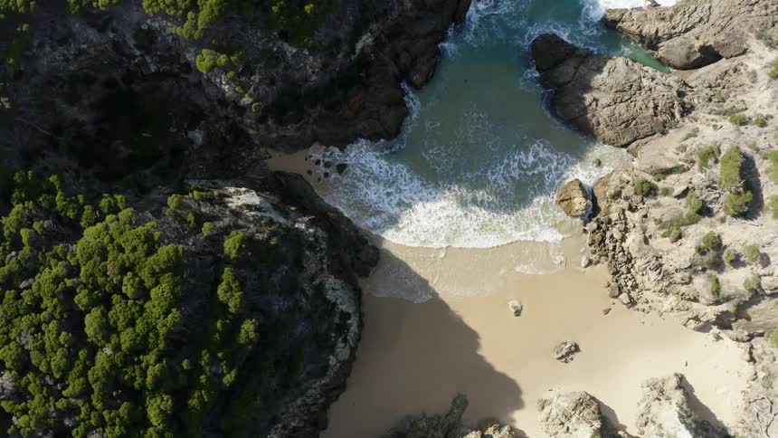 The tide washes onto a narrow beach nestled between tall rock and trees