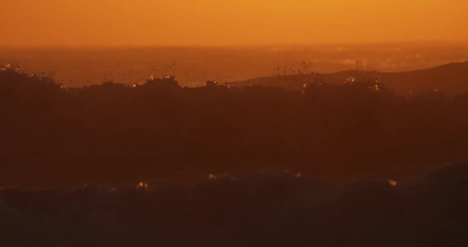 Waves crashing in an ocean with an orange sky at sunset