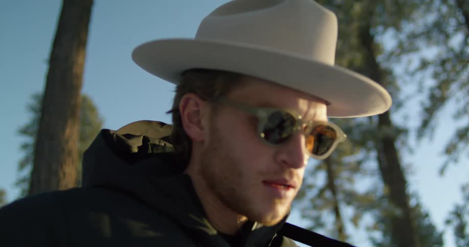 Man wearing hat and sunglasses stands in forest singing