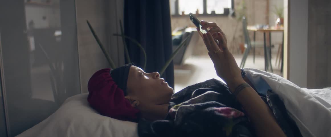A woman scrolling on a smartphone while lying in bed at home