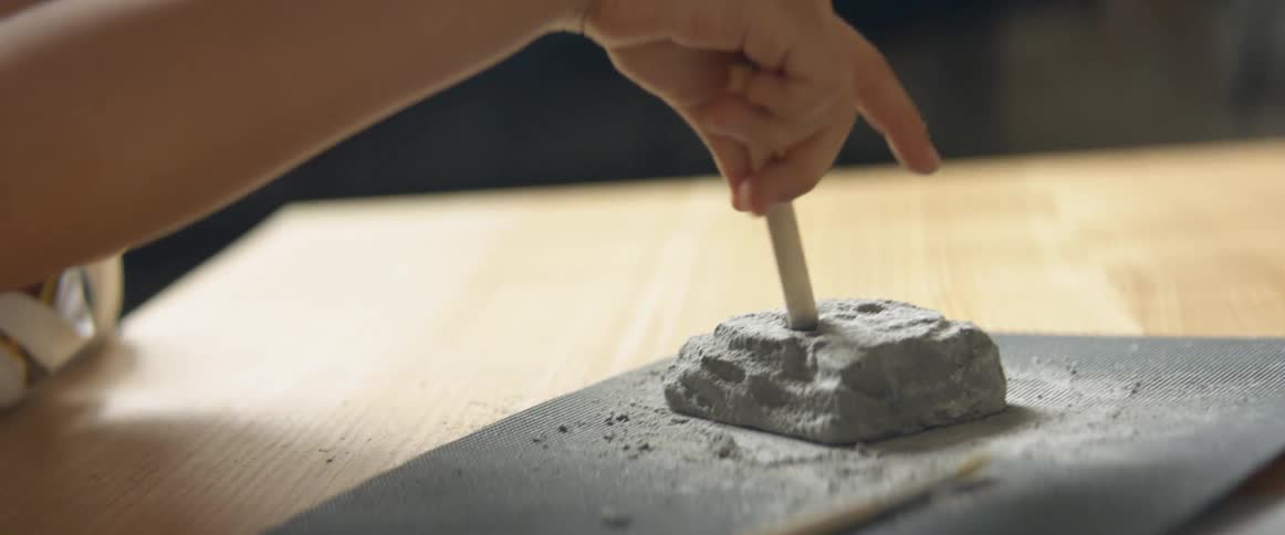 A young boy sits at a table and twists a pencil into clay