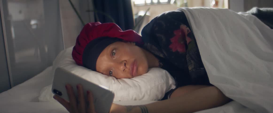 A woman lays in bed watching something on her cell phone