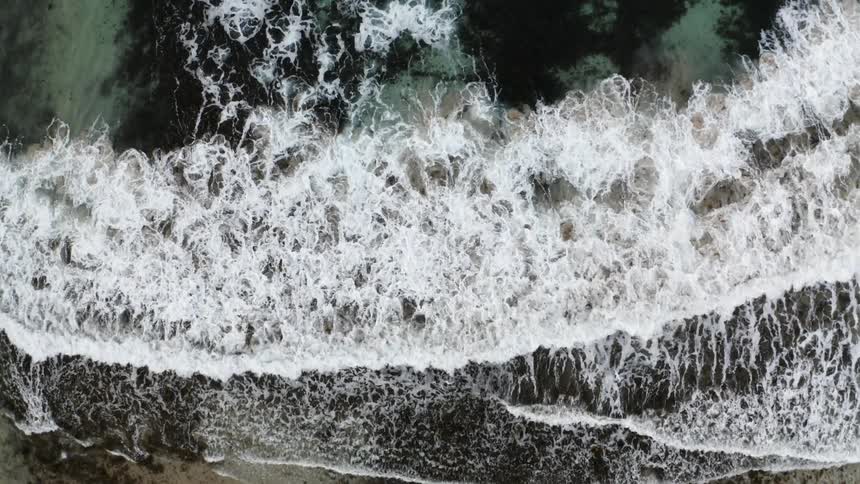 Aerial view of ocean waves crashing on the shoreline of a beach