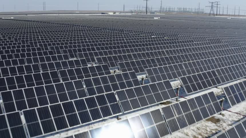 Solar farm with many solar panels with snow on the ground and utility towers in the distance