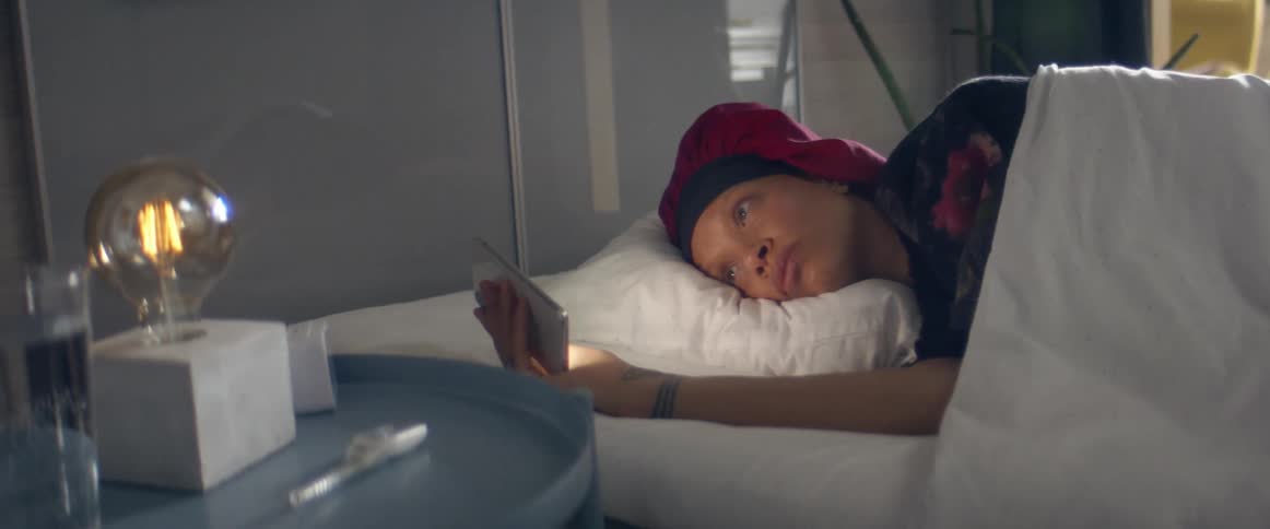 Woman with a red bonnet lies in bed and looks at the smartphone in the bedroom