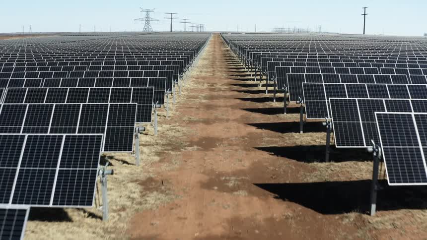 A landscape with solar panels with utility poles the sky and clouds in the background