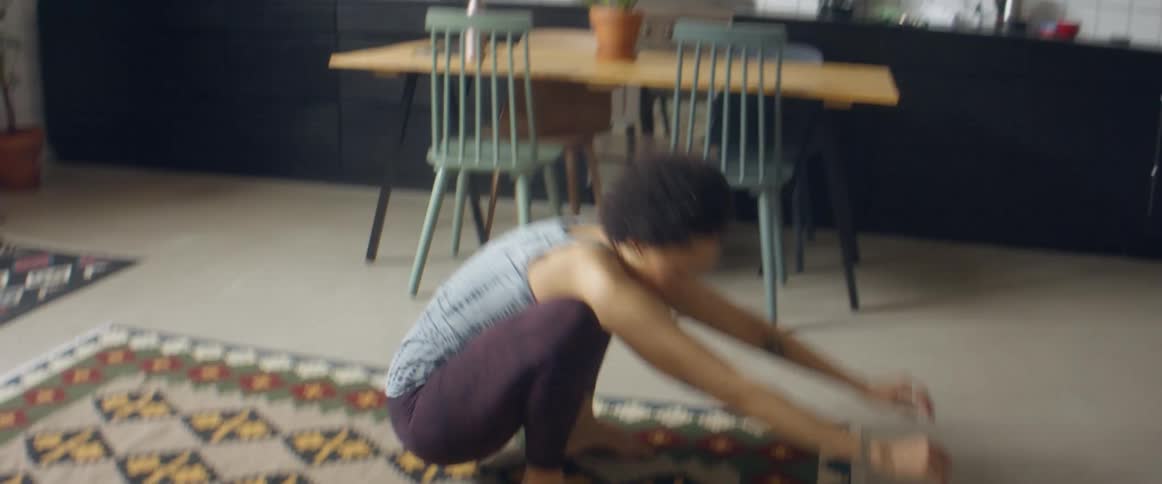 A woman at home takes a drink of water and then lies on the floor to exercise