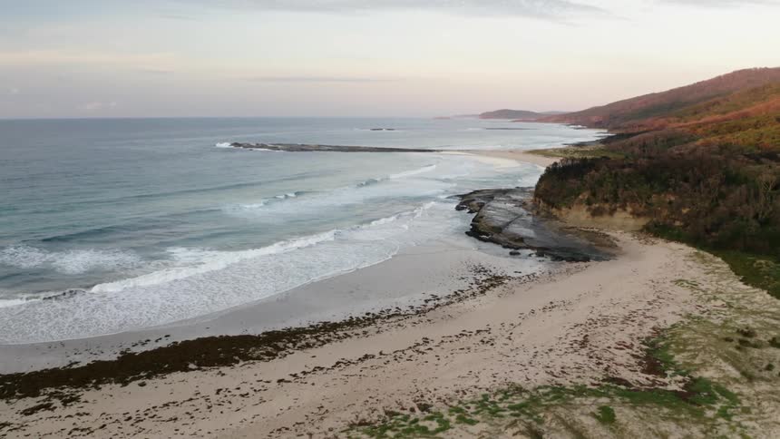 Waves roll in over a beach with a mountain in the distance