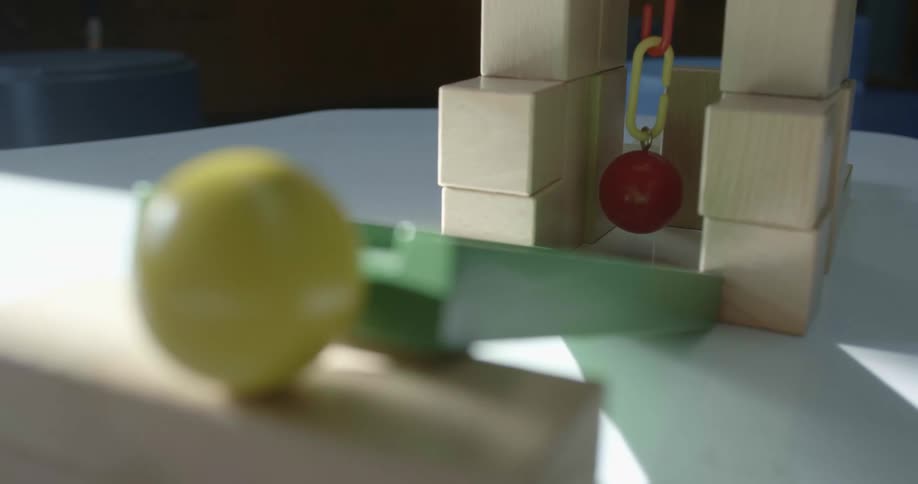 Ball is seton stacked wooden blocks near green ramp pointed toward ball hanging between stacked wooden blocks