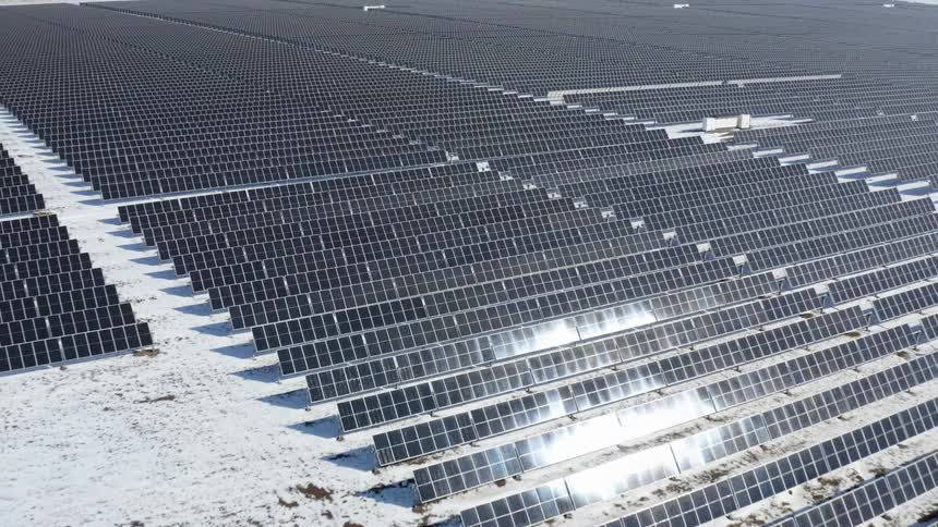 Rows of solar panels at solar farm sit on snow covered field reflecting the sun