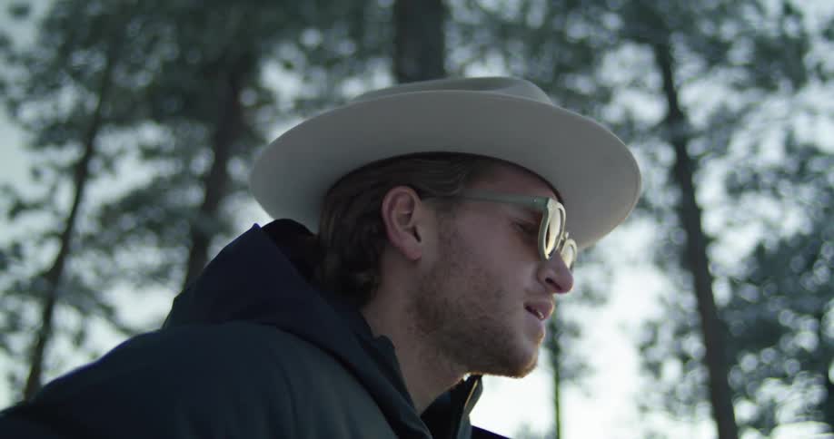 A man with a hat and sunglasses singing with trees the sky and clouds in the background