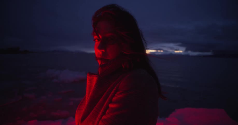 Woman looking at the camera stands in a field at night lighted by a red light