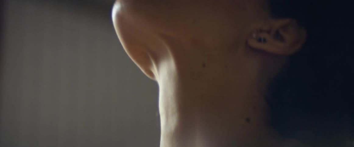A woman with a nose ring in a room stretching with a wall in the background