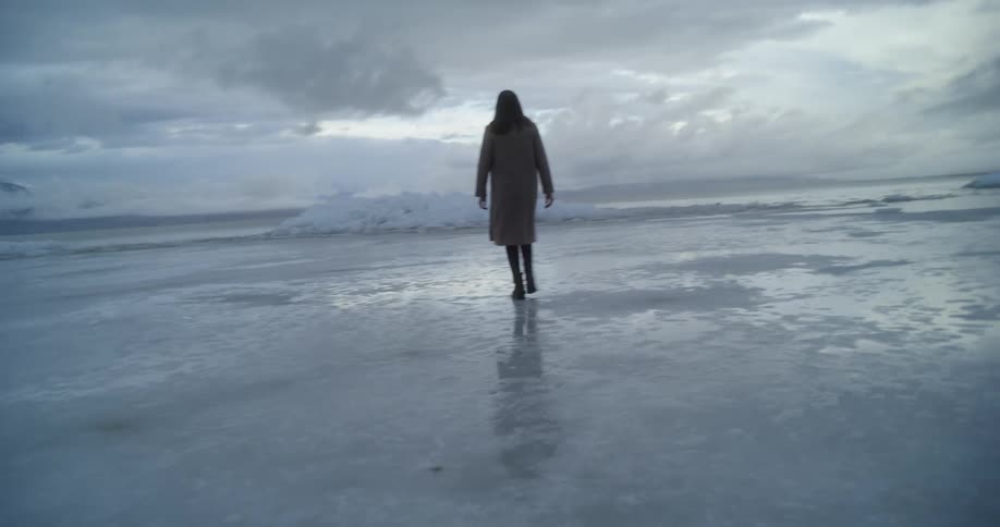 Woman with brown hair and an overcoat walks on ice lake