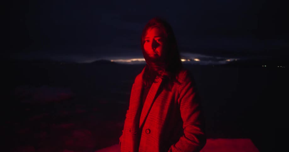 Woman stands outdoors at night lit by red blinking light