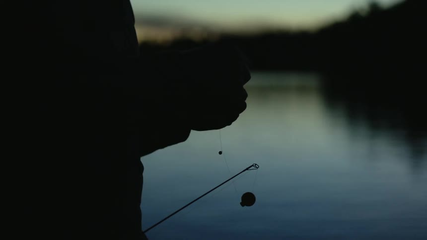 A man stands on the shore and puts a hook on a fishing line