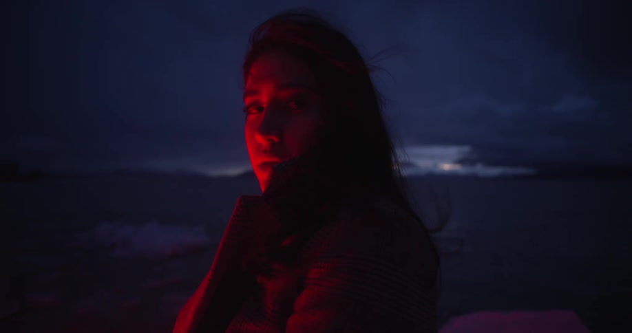 Woman looking at the camera stands in near a lake at night lighted by a red light