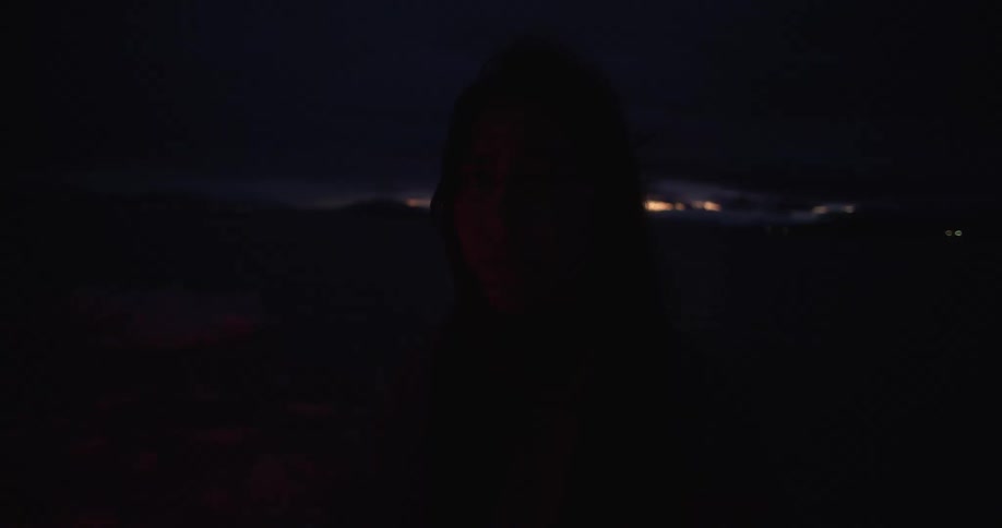 A red light flashes on and off of the face of a woman standing outdoors staring at the camera at night time