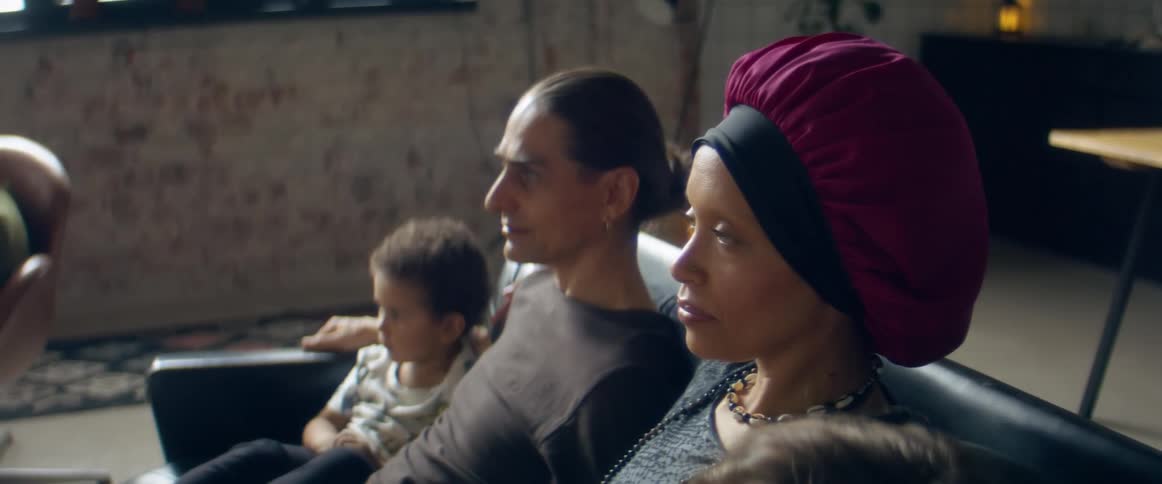 A mother sitting on a couch with her husband and two children watching television during the day