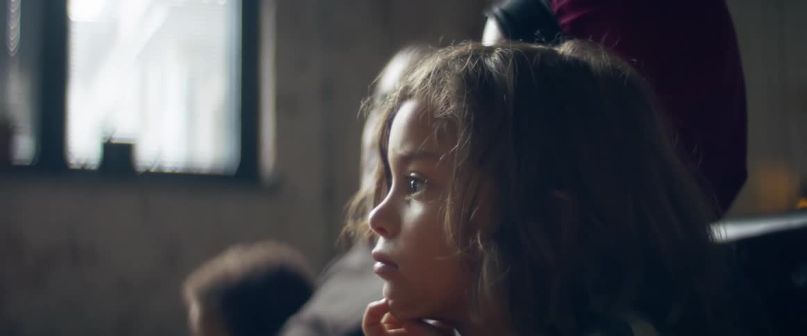 A little boy sits with his family on a couch in a living room watching tv