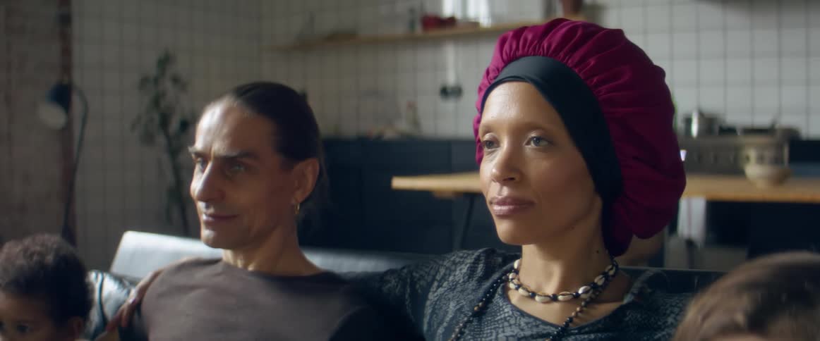 A mother and father sit on a couch near the kitchen with their children