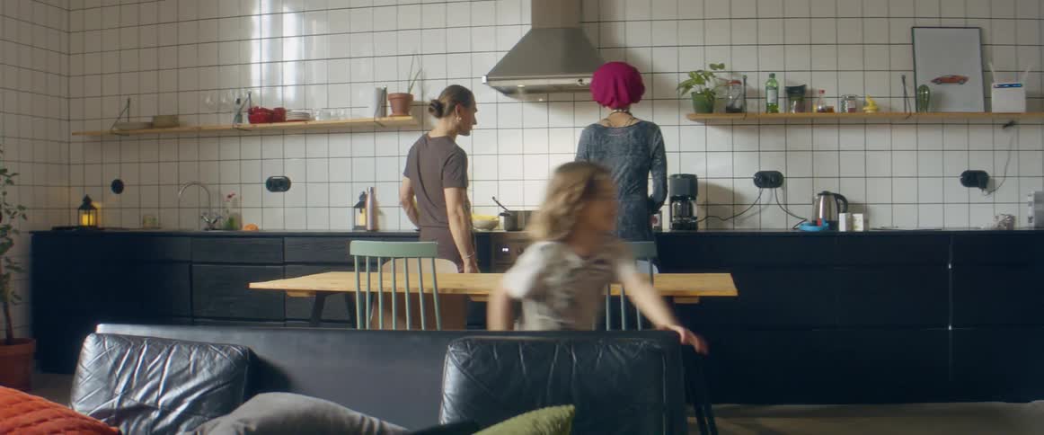 A man and woman talk in the kitchen as they cook and two little boys run around