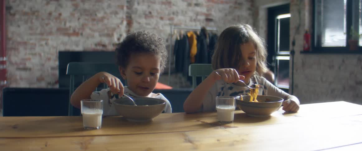 Two boys sitting on chairs at a table eating spaghetti