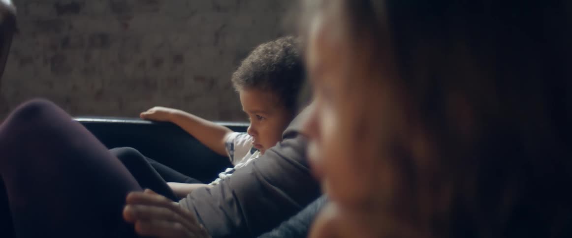 A little boy at home sits in his fathers lap next to his mother and brother