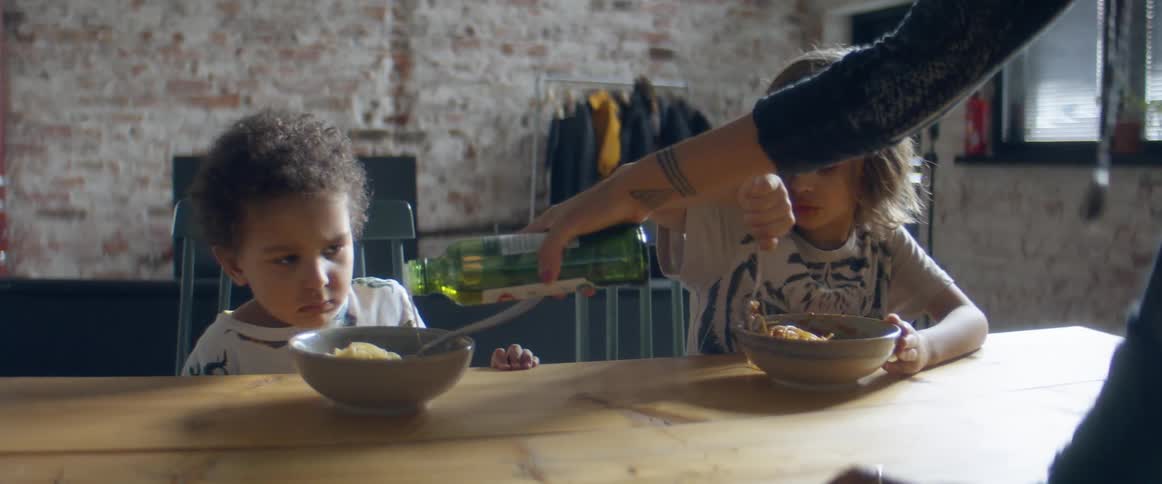 A woman adding oil to her sons' spaghetti