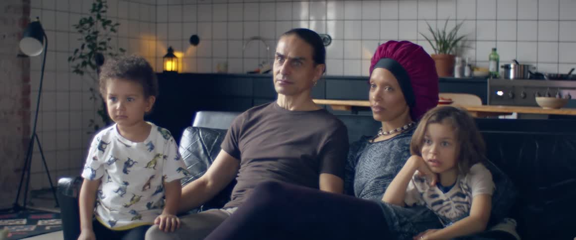 Parents with their children sitting side by side on the black sofa watching television